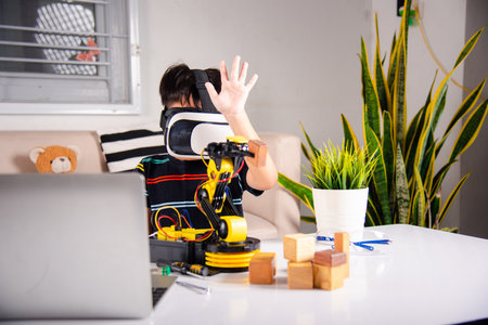 Asian kid boy using VR glasses on robotic arm in workshop, Child learning programer control robot arm with sensors to pick up wood block, Technology education, Virtual Reality Simulator, industry 4.0の写真素材