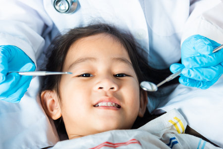 Dental kid health examination. Doctor examines oral cavity of little child uses mouth mirror to checking teeth cavity, Asian dentist making examination procedure for smiling cute little girlの写真素材
