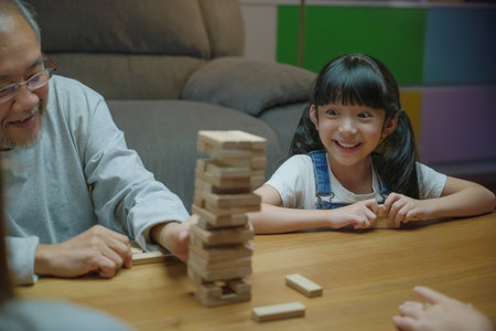 Happy grandparents Asian family enjoy playing toy block with little daughter and mother together at home night time, Smiling parent having fun play build constructor tower of wooden blocks, educationの写真素材