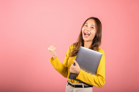 Portrait of happy Asian beautiful young woman confident smiling face holding laptop computer raise...