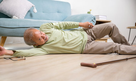 Asian old man lying on floor after falling down with wooden walking stick, Sick senior man beside couch on rug in living room at home, Elderly having an accident after doing physical therapy aloneの写真素材