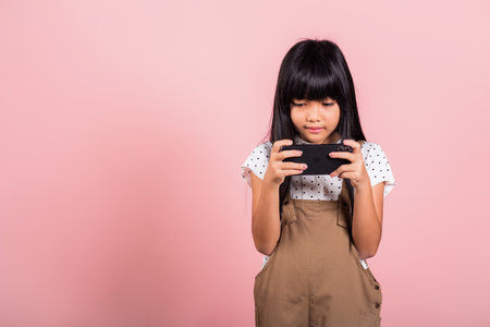 Asian kid 10 years enjoying using mobile phone for social network media at studio shot isolated on pink background, Happy child girl lifestyle using smartphone, playing gamesの写真素材