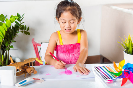 Happy child little girl colorful drawing pink heart on white paper, Asian cute kid preschooler smiling draw color love picture card at home, Valentines or Mothers Day or Fathers Dayの写真素材