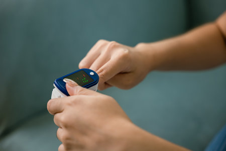 Young woman using pulse oximeter to monitor blood oxygen levels and pulse rate on finger under sofa in living room at home, Self healthcare with coronavirus pandemic, medical healthcare conceptの写真素材