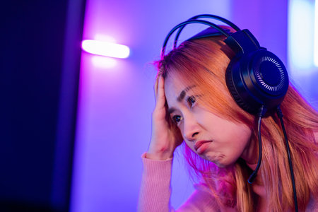 Game Over. Asian gamer playing online video game she losing and sad on computer PC colorful neon LED lights, young woman in gaming headphones feeling disappointed about lost game, E-Sport conceptの写真素材