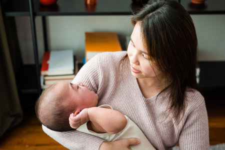 Asian mom holding her crying little baby at home, Mother comforts little son or daughter newborn, Parent woman cuddling baby tenderness, cry after birthの写真素材