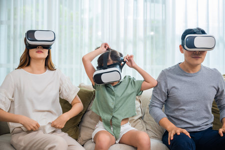 Asian family wear vr glasses headsets sitting on sofa in living room, game entertainment innovation technology, Happy family have mother father and daughter watching movie or playing video gameの写真素材