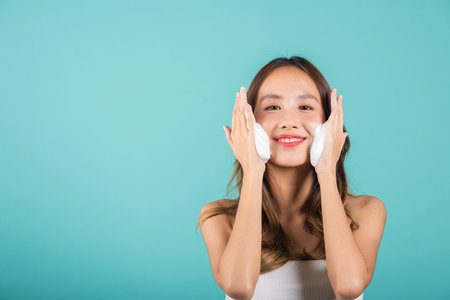 Portrait beautiful female smile applies foaming cleanser healthy skin, Asian women face wash exfoliating scrub soap with skincare cleansing, Studio isolated on blue background, skincare daily routineの写真素材
