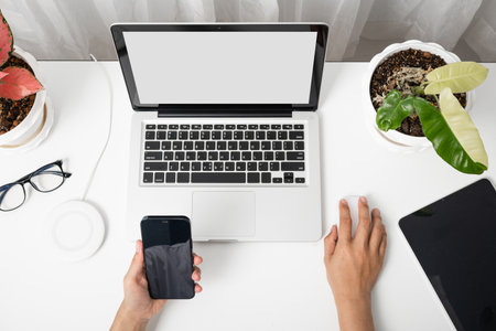 Female sitting workspace using hand holding black smartphone blank screen mock up on a table with laptop computer, female hold mobile phone with notebook at officeの写真素材