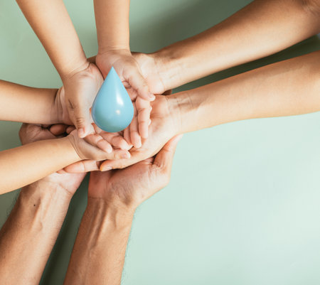 Hands of family holding 3D blue water drop, father mother and child hand stack holding drop clean water together studio shot isolated on blue background, world of water day, CSR, save earth conceptの写真素材