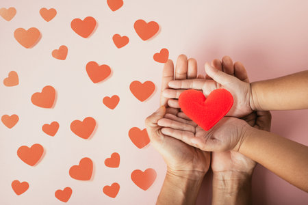 Love and Valentines Day background. Top view flat lay of paper elements cutting red heart holding on palms of father, mother and child together on pink background, Banner of family holidayの写真素材