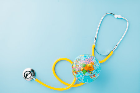 World Health Day. Top view yellow doctor stethoscope wrapped around world globe isolated on pastel...