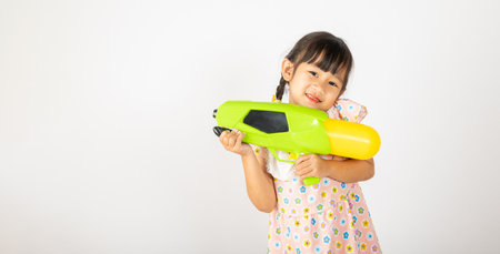 Happy Songkran Day, Asian little girl holding plastic water gun, Thai child funny hold toy water pistol and smile, isolated on white background, Thailand Songkran festival national culture conceptの写真素材