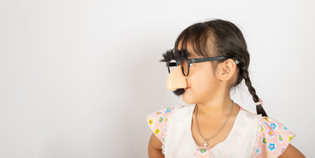 April Fools Day. Portrait of Funny kid little girl clown wears a big nos and glasses and has a mustache isolated on white background with copy space, Happy smile child festive decorの写真素材