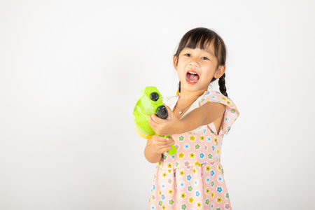 Happy Songkran Day, Asian little girl holding plastic water gun, Thai child funny hold toy water pistol and smile, isolated on white background, Thailand Songkran festival national culture conceptの写真素材