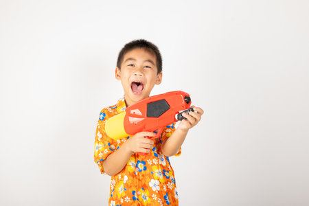 Happy Songkran Day, Asian kid boy with floral shirt hold water gun, Thai child funny hold toy water pistol and smile, isolated on white background, Thailand Songkran festival national culture conceptの写真素材