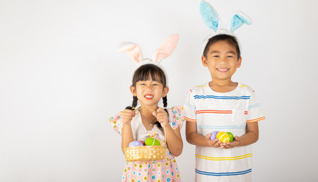 Happy Easter Day. Two smile Asian little girl and boy wearing easter bunny ears holding basket with eggs isolated on white background with copy space, Happy family children in holidayの写真素材