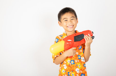 Happy Songkran Day, Asian kid boy with floral shirt hold water gun, Thai child funny hold toy water pistol and smile, isolated on white background, Thailand Songkran festival national culture conceptの写真素材