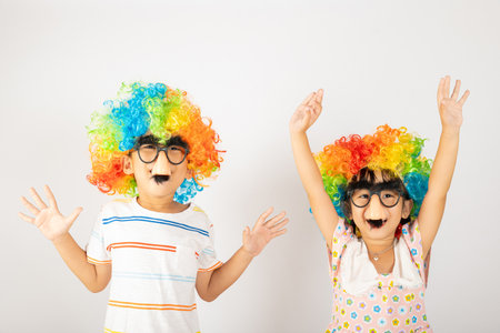 April Fools Day. Two brothers funny kid little girl clown wears curly wig colorful big nos and glasses and has mustache playing fool isolated on white background copy space, Happy child festive decorの写真素材