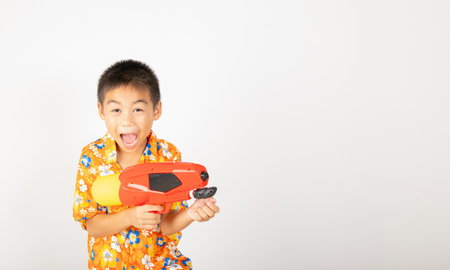 Happy Songkran Day, Asian kid boy with floral shirt hold water gun, Thai child funny hold toy water pistol and smile, isolated on white background, Thailand Songkran festival national culture conceptの写真素材