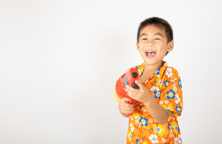 Happy Songkran Day, Asian kid boy with floral shirt hold water gun, Thai child funny hold toy water pistol and smile, isolated on white background, Thailand Songkran festival national culture conceptの写真素材