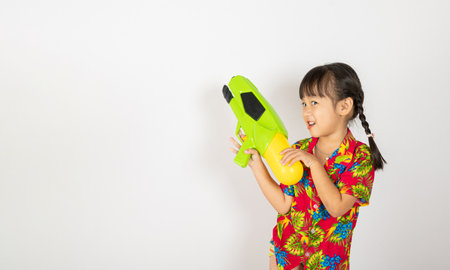 Happy Songkran Day, Asian kid girl with floral shirt hold water gun, Thai child funny hold toy water pistol and smile, isolated on white background, Thailand Songkran festival national culture conceptの写真素材