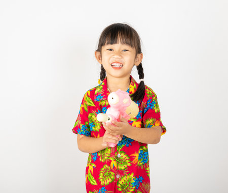 Happy Songkran Day, Asian kid girl with floral shirt hold water gun, Thai child funny hold toy water pistol and smile, isolated on white background, Thailand Songkran festival national culture conceptの写真素材