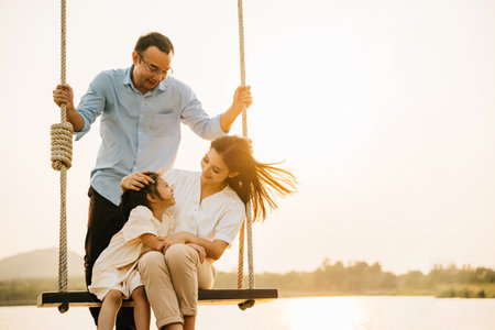 A happy family playing together on a swing set in a beautiful park, with the parents and children laughing and smiling in the sunshine, Happy Family Dayの写真素材