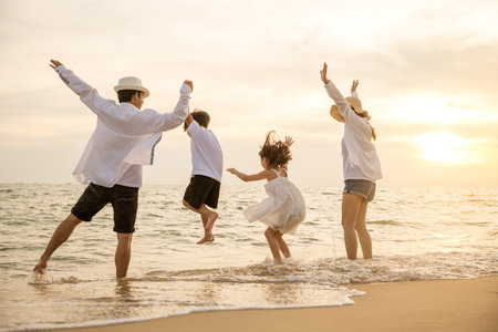 Happy Asian family have fun jumping together on beach in holiday at sunset time, Silhouette of family holding hands live healthy lifestyle on beach, back people enjoying travel and vacations conceptの写真素材