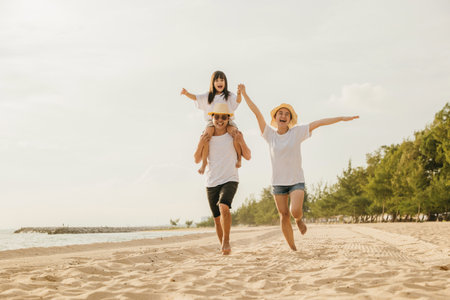 Road trips day. Happy family people having fun in summer vacation on beach, daughter riding on father back and mother running race at sand beach, enjoying road family trip playing together outdoorの写真素材