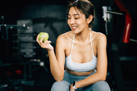 An Asian woman holding a green apple in a fitness gym, reminding viewers of the importance of a healthy diet for maintaining a fit and toned body. healthy lifestyle bodybuildingの写真素材