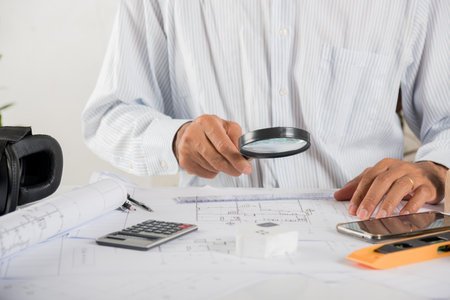 Architectural interior designer working holding magnifying glass and look on blueprint in working...