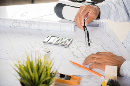 Architect workplace. Architectural building design and construction plans with blueprints paper project plans and VR glasses, designing man edit a building or architecture drawing with compass dividerの写真素材