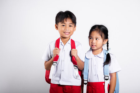 Two Asian student kid girl boy schoolchildren brother sister smile happy wear student thai uniform red pants skirt in studio shot isolated on white background, Portrait little children girl preschoolの写真素材