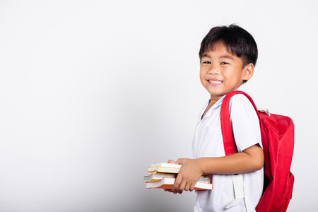 Asian adorable toddler smiling happy wearing student thai uniform red pants stand books for study ready for school isolated on white background, Portrait little children boy preschool, Back to schoolの写真素材