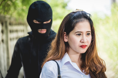 The robber holding a knife Is going to rob on back her while women are talking on mobile phone, Thieves were threatened following woman on the way she was walking homeの写真素材