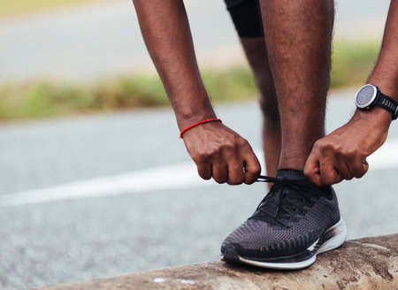 Close up Asian sport runner black man wear watch stand step on the footpath trying shoelace running shoes getting ready for jogging and run outdoor street health park, healthy exercise workout conceptの写真素材