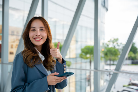 Portrait of a smiling woman holding a cellphone and giving a thumbs up gesture, digital communication concept.の写真素材