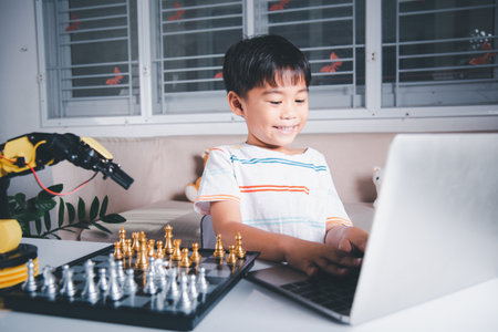 Asian little boy programming code to robot machine arm on laptop for play chess, STEM education E-learning, Funny children learning getting lesson control robot arm, Technology science educationの写真素材