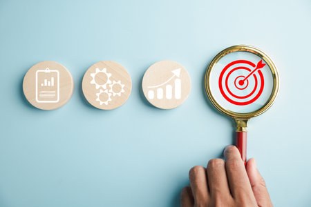 The magnifying glass aids a businessman in focusing on the target goal icon, symbolizing his...