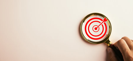 A magnifier glass highlights a target board for focused business objectives. With a background and...