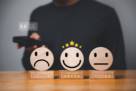Mans hand selects the best smiley face on a wooden block circle to rate excellent business services and customer experience. Satisfaction survey concept.の写真素材