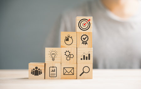 Wooden cube block step on a table with Action Plan, Goal, and Target icons. Success and business target concept. Project management and company strategy symbolize growth.の写真素材