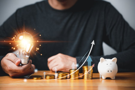 Hand holding a light bulb with coins stack and chart graph, representing creative concept of saving money and investing in wealth. Financial background for business accounting. innovative and bright.の写真素材