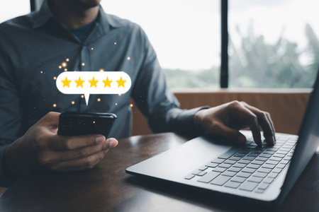 Client feedback is essential for business growth. A mans hand holding a laptop and smartphone with a 5-star rating icon for service excellence and satisfaction surveyの写真素材