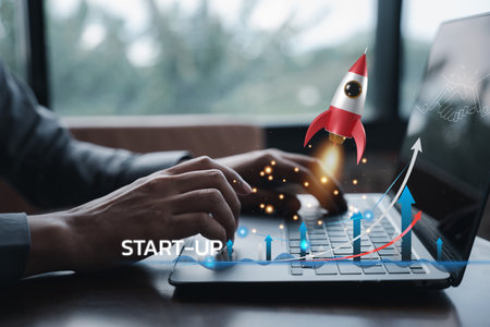 A businessman controls the white rocket icon, launching it into space from his laptop for a global startup business concept on the modern virtual interface.の写真素材