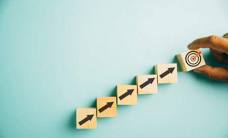 Wooden blocks with a prominent Target icon and rise up arrows. Bar graph chart steps illustrate business growth on a blue background. Represents profit, investment, and economic improvement concepts.の写真素材