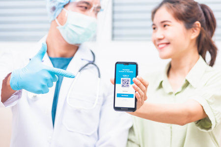 Asian young woman in medical mask show app smartphone mobile digital screen vaccinated coronavirus (COVID-19) certificate after getting vaccine prevent and doctor pointing to confirm certificateの写真素材