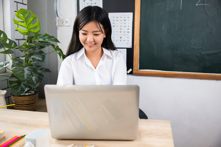 Back to school. Portrait of young woman teacher with laptop at desk in classroom, Smiling female...