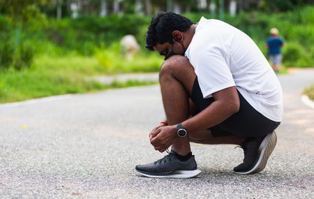 Close up Asian sport runner black man wear watch sitting he trying shoelace running shoes getting ready for jogging and run at the outdoor street health park, healthy exercise workout conceptの写真素材